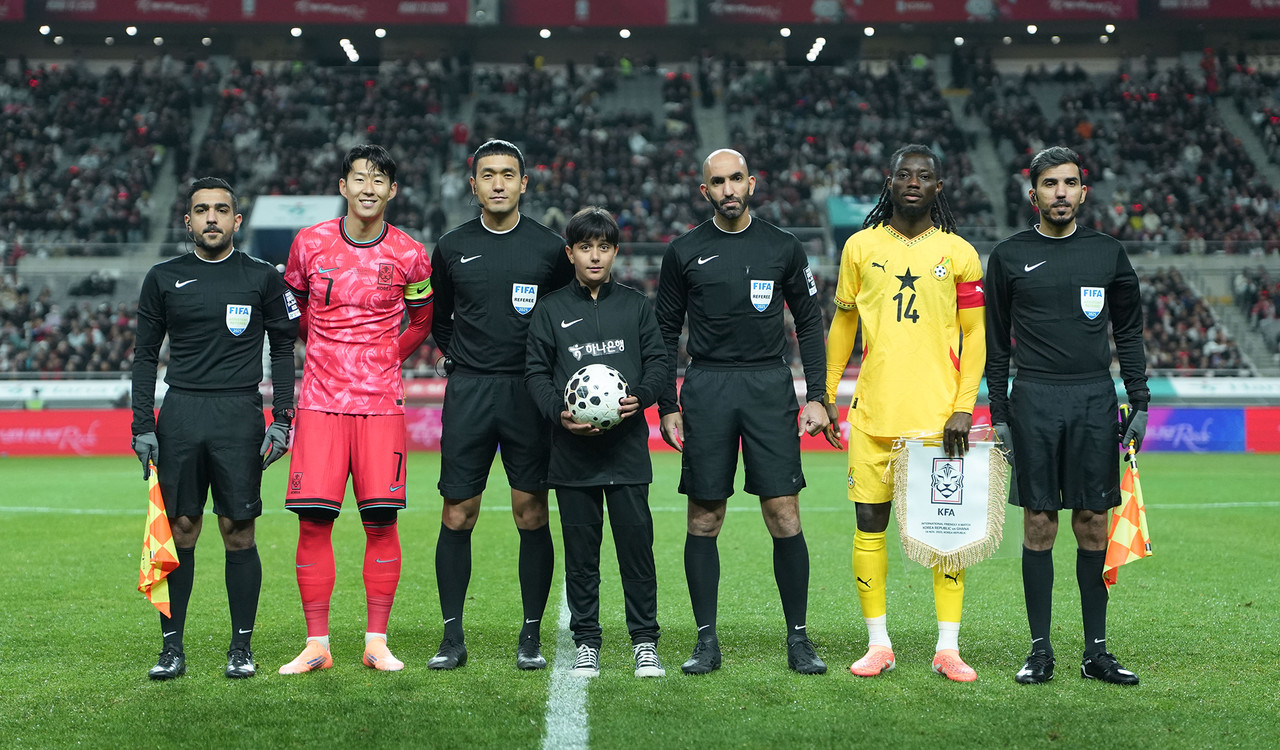 하나은행은 지난 18일 서울월드컵경기장에서 열린 대한민국과 가나의 축구 국가대표팀 A매치 경기에서 이주배경 가정 아동·청소년들에게 '매치볼 키드'와 '기수단'으로 참여할 수 있는 특별한 체험 기회를 제공했다고 밝혔다.이날 경기 시작에 앞서 아프가니스탄 출신 '매치볼 키드' 마시(Masih)가 양 팀 주장 및 심판진과 함께 기념촬영을 하고 있다. / 사진=하나은행