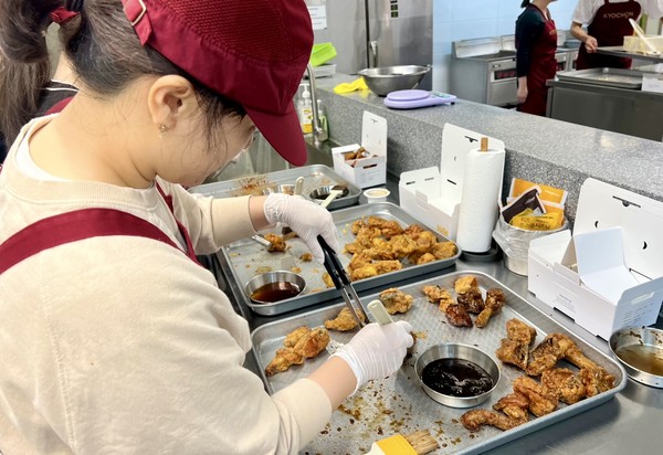 경기도 오산시의 교육 및 R&D센터 정구관(교촌 아카데미) 내 브랜드 체험관에서 열린 '교촌1991 소비자 캠프'에서 참여자들이 양념을 일일이 치킨에 붓으로 바르고 있다. 양념 붓질은 교촌치킨의 독특한 조리법으로 브랜드 시그니처로 여겨진다. 교촌치킨은 최근 일부 메뉴의 조리 방식을 붓질에서 텀블링(치킨을 양념에 버무리는 것)으로 변경한다고 발표했다가 여론의 뭇매를 맞고 붓질 도포로 되돌리겠다고 공식화했다. / 사진=교촌치킨